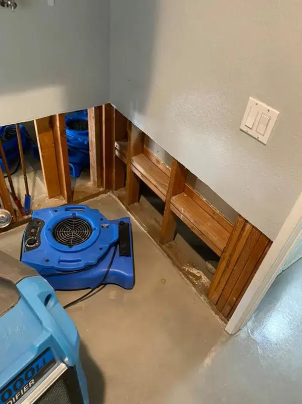 Air movers aimed at an opened cabinet base and wall during a Highland dry-out
